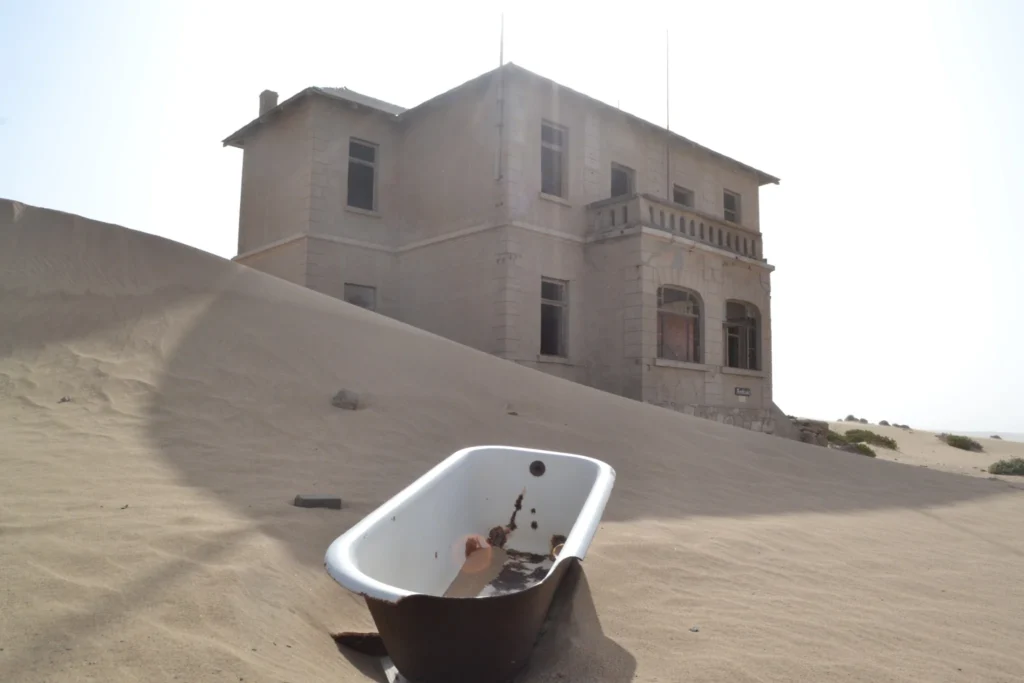 Vecchia vasca da bagno nella sabbia davanti a una casa abbandonata di Kolmanskop